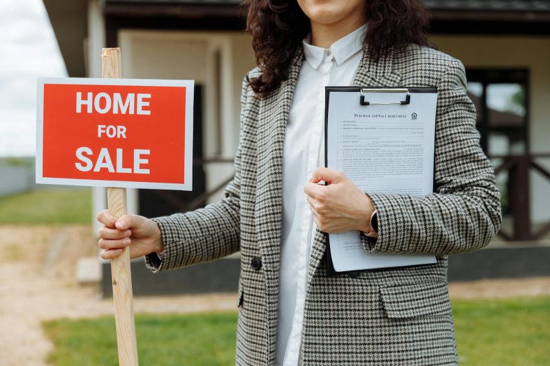 Great Falls, Montana Branch 7 A real estate agent holding a home for sale sign and clipboa 1779814844